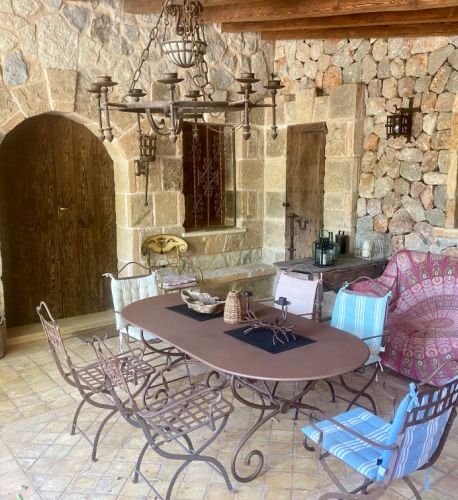The covered terrace dining area: a long iron table and chairs against rough stone walls under a forged candle chandelier.