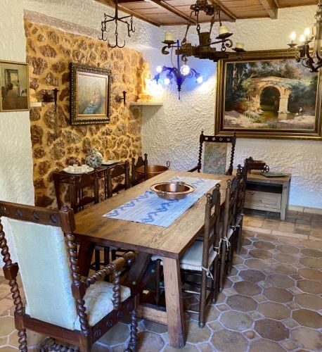 The formal dining room: a long wooden table and carved high-back chairs against an exposed stone wall hung with paintings.
