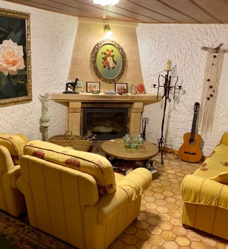 A snug sitting room with a stone fireplace, deep yellow sofas and a guitar resting in the corner.