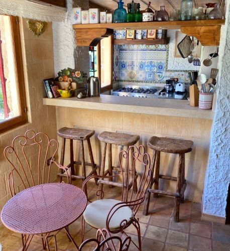 A small kitchen and breakfast bar with hand-painted Mallorcan tiles, timber stools and a pink café table.