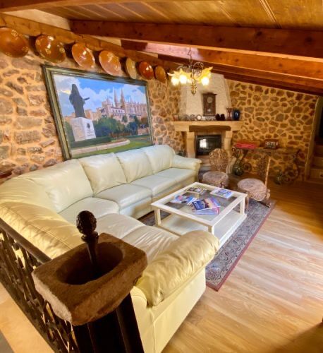 An upstairs sitting room with cream leather sofas, exposed stone walls and beamed ceiling, a painting of Palma cathedral above.