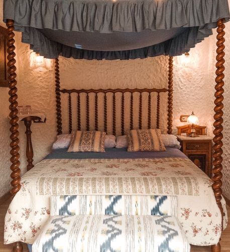 A whitewashed bedroom with a spiral-column four-poster bed and a patterned bench at its foot.
