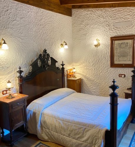 A bedroom with thick limewashed stone walls, twin brass lamps and a carved dark-wood headboard.