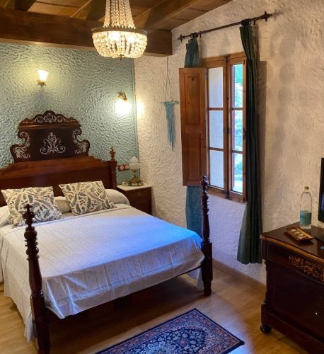 A bedroom with a sage-green wall, a carved four-poster bed, a glass chandelier and a shuttered window onto the garden.