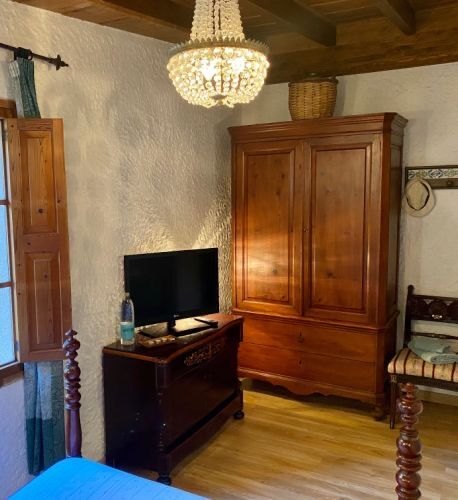 A bedroom corner with a cherry-wood armoire, a glass chandelier and beamed ceiling.