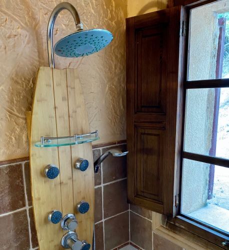 A walk-in shower with a bamboo rain-column against terracotta tiles, beside a deep timber window.